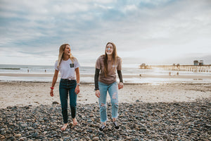 Two girls are walking on the beach. They are smiling and have colorful, reef safe sunscreen on their noses.